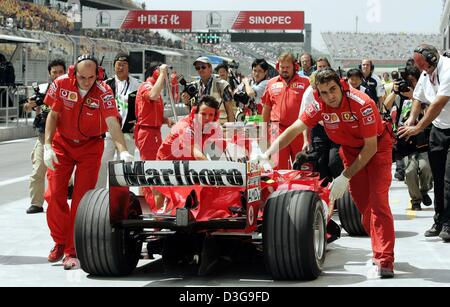 (Afp) - la mécanique de Ferrari pousser la voiture de course de l'Allemand sept-fois champion de Formule 1 Michael Schumacher de retour dans la fosse pendant la formation gratuite à la nouvelle race course à Shanghai, Chine, le 24 septembre 2004. La course de dimanche sera la première fois qu'un Grand Prix est organisé en Chine. Banque D'Images