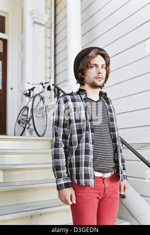 Les gens branchés et Beatniks - un jeune homme hipster en jeans serré, chemise à carreaux, et un chapeau sur le point de quitter la maison dans son vélo à engins fixes. Banque D'Images