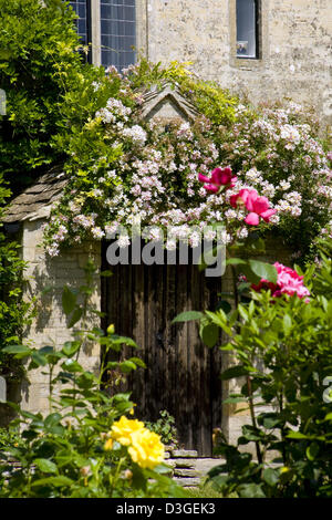 Une vieille maison en pierre avec des rosiers grimpants sur la porte, Gloucestershire, England, UK Banque D'Images