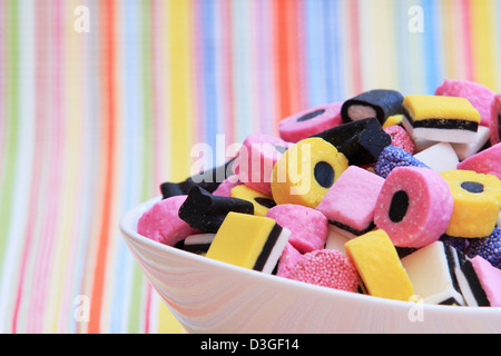 Partie d'un bol blanc plein de bonbons à la réglisse, contre un fond coloré Banque D'Images