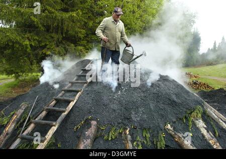 (Afp) - Peter Behringer se dresse sur un mont et verse de l'eau sur le charbon incandescent dans Feldberg-Altglashuetten, Allemagne, 16 juin 2004. C'est une façon traditionnelle de fabrication du charbon qui a été largement utilisé dans le passé. Il faut environ 14 jours pour le processus de production du charbon de bois de haute qualité fabriqués à partir de bois. Banque D'Images