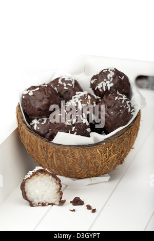 Avec le lait de coco recouvert de chocolat doux-amer truffes de riz dans un demi-coque de noix de coco sur un plateau en bois Banque D'Images