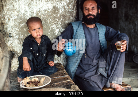 Père et fils de réfugiés afghans à manger une friterie. Peshawar, Pakistan Banque D'Images