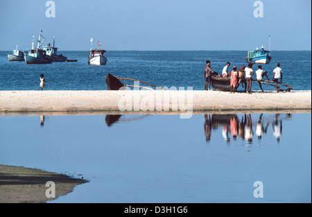 De petits bateaux de pêche amarrés au large de la côte et des pêcheurs reposant sur la plage, se reflétant dans une réflexion dans l'eau fixe. Goa, Inde Banque D'Images