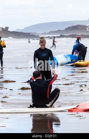 Une femme vient en aide à un homme fatigué de se tenir après le surf sur Widemouth plage, près de Bude, Cornwall, UK Banque D'Images