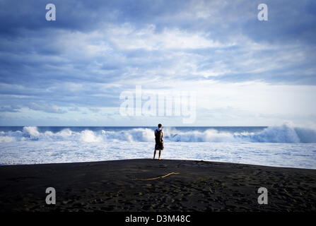 L'homme pose sur l'anse de sable noir au coucher du soleil, à l'Est de Palm Hôtel, Petit Ile, l'île de la réunion, en français, de l'Océan Indien Banque D'Images