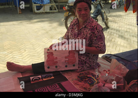 La broderie d'une femme se trouve dans la lueur rose du marché une tente au marché Hmong à Luang Phrabang Banque D'Images