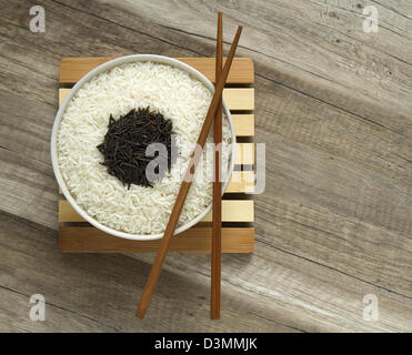 Deux variétés de riz blanc, dans une cuvette ronde et noir dans une cuillère en bois brun avec des baguettes. Banque D'Images