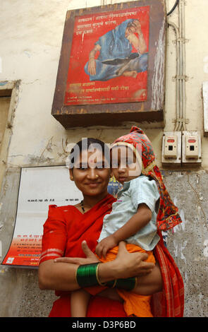 (Afp) - une jeune mère avec son petit garçon dans ses bras devant une affiche montrant une mère et son enfant mort et mettant en garde les mères à venir à l'hôpital lorsque leurs enfants tombent malades dans un hôpital de Bombay, Inde, 04 juillet 2006. Photo : Wolfgang Langenstrassen Banque D'Images