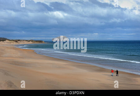 Un couple marche sur le long de la plage déserte Tyningham vers la Bass Rock dans la distance, North Berwick, en Écosse. Banque D'Images