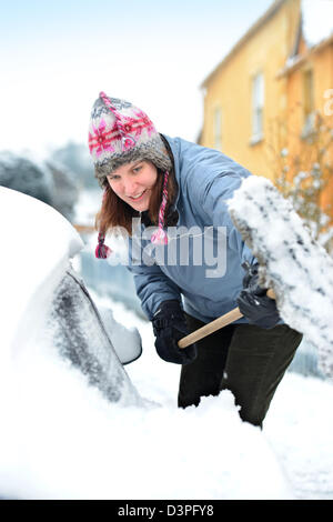 Un automobiliste s'efface la neige de sa voiture dans le village de Badminton Gloucestershire UK Banque D'Images