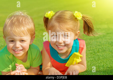 Photo de petit frère et sœur couchée sur l'herbe verte champ dans journée ensoleillée, deux adorables enfant jouant sur l'arrière-cour, Banque D'Images