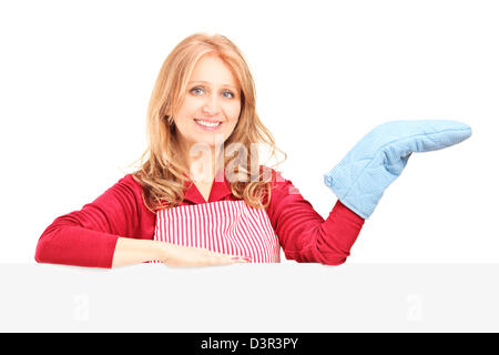 Smiling woman in apron posant avec une mitaine de cuisine derrière un panneau isolé sur fond blanc Banque D'Images