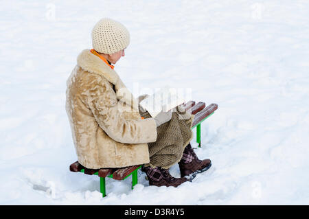 Femme assise sur un banc et la lecture d'un livre en hiver. La neige. Banque D'Images