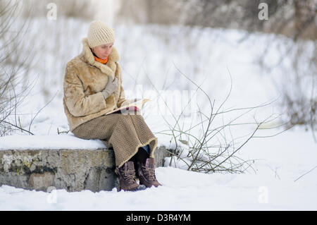 Femme assise sur un banc et la lecture d'un livre en hiver. La neige. Banque D'Images