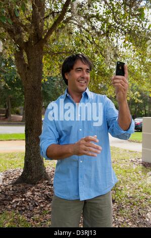 Homme d'âge moyen 40 ans mixed race holding iPhone prend en photo terrain plein air d'accueil arbre en retour wearing blue shirt Banque D'Images