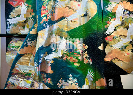 Kimono de mariage de printemps sur l'affichage a les représentations de fleurs de cerisier et de grues japonaises contre un fond coloré. Banque D'Images