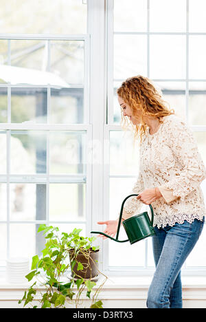 Smiling woman watering plante verte à la maison par fenêtre Banque D'Images