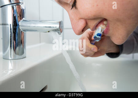 Femme est se brosser les dents, tandis que l'eau est toujours en cours d'exécution du robinet. Image symbole pour le gaspillage d'eau. Banque D'Images