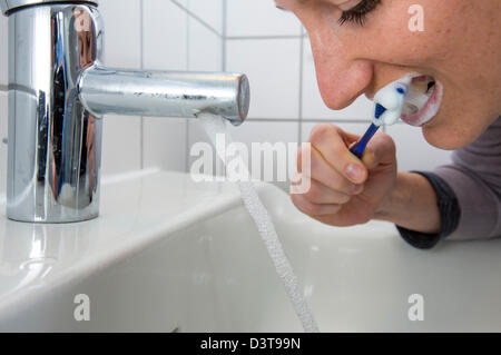 Femme est se brosser les dents, tandis que l'eau est toujours en cours d'exécution du robinet. Image symbole pour le gaspillage d'eau. Banque D'Images