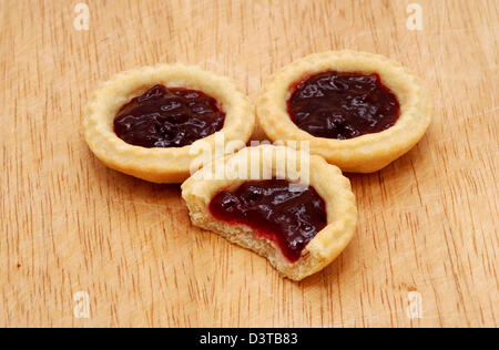 Trois délicieuses tartelettes à la confiture, un avec un morceau tiré de elle, sur une table en bois Banque D'Images