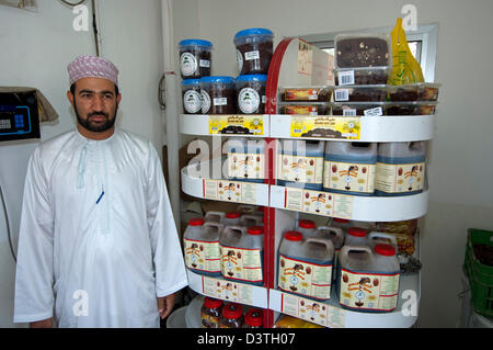 Comité permanent du vendeur dans un magasin à côté d'un rayon avec les produits de la marque date Date d'or, Rustaq, Sultanat d'Oman Banque D'Images