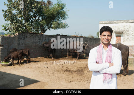 Farmer standing dans un hangar avec des buffles d'eau (Bubalus bubalis) dans l'arrière-plan, Sonipat, Haryana, Inde Banque D'Images