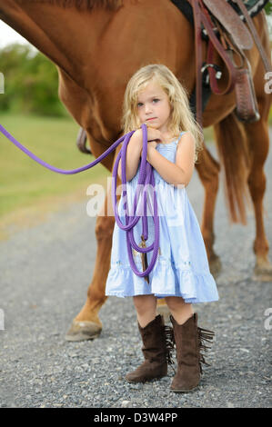 Petite fille blonde debout à côté d'un grand cheval tout en maintenant la ligne de sonde. Banque D'Images