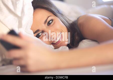 Happy woman lying on bed smiling pendant la lecture d'un message texte à partir de quelqu'un Banque D'Images