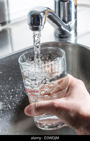 L'eau coule dans un verre, à partir d'un robinet dans une cuisine. Banque D'Images