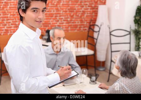 Jeune serveur approche d'un couple plus âgé pour prendre leur commande dans un restaurant. Banque D'Images