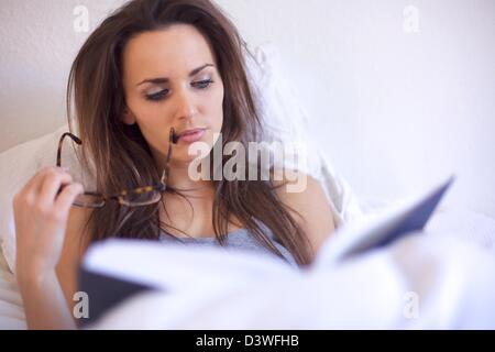 Brunette woman absorbé par la lecture d'un livre alors que dans sa chambre Banque D'Images