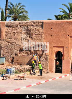 Ouvriers effectuant des réparations sur la chaussée devant les vieux murs de la ville en brique de boue rose rougeâtre de Marrakech, Maroc, Afrique du Nord Banque D'Images