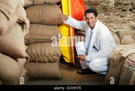 L'homme accroupi près de la pile de sacs de blé, Anaj, Mandi, Sohna Gurgaon, Haryana, Inde Banque D'Images