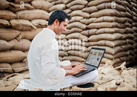 Homme assis sur le sac de blé et à l'aide d'un ordinateur portable dans un marché des céréales, l'Anaj, Mandi, Sohna Gurgaon, Haryana, Inde Banque D'Images