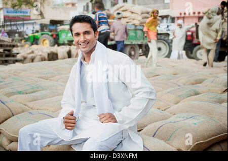 Homme assis sur pile de sacs de blé dans un marché des céréales, Anaj, Mandi, Sohna Gurgaon, Haryana, Inde Banque D'Images