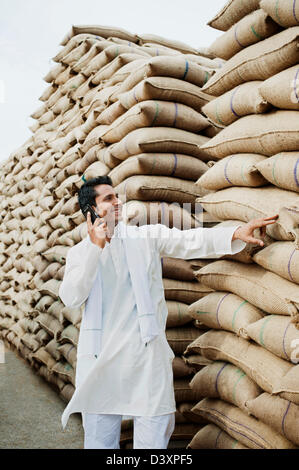 Homme debout près de sacs de blé et de parler sur un téléphone mobile, l'Anaj, Mandi, Sohna Gurgaon, Haryana, Inde Banque D'Images