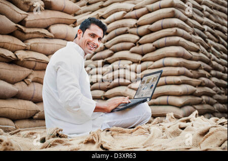 Homme assis sur le sac de blé et à l'aide d'un ordinateur portable dans un marché des céréales, l'Anaj, Mandi, Sohna Gurgaon, Haryana, Inde Banque D'Images