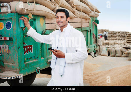 Homme debout près d'une remorque holding a mobile phone, Anaj, Mandi, Sohna Gurgaon, Haryana, Inde Banque D'Images