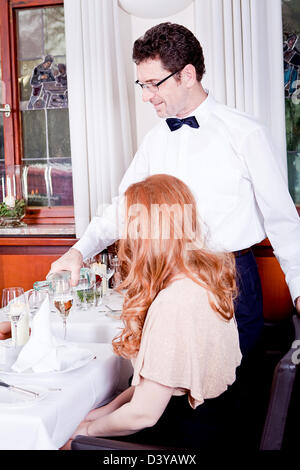 L'homme et la femme pour le dîner au restaurant waiter serving eau minérale Banque D'Images