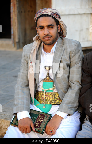 Jeune homme assis portant des vêtements traditionnels, y compris Jambiyya, et Coran Banque D'Images