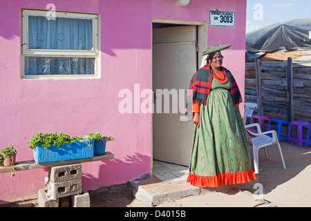 Femme Herero en robe colorée traditionnelle devant sa maison dans le township près de Swakopmund, Namibie, Afrique du Sud Banque D'Images