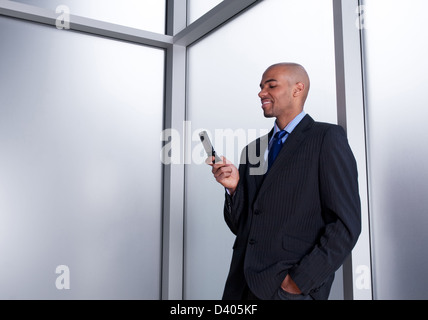 Jeune homme d'à côté d'une fenêtre de bureau à la recherche de son téléphone cellulaire, en souriant. Banque D'Images