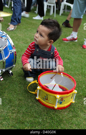 C'est une photo d'un jeune enfant garçon qui joue de la batterie sur un jouet enfant instrument musique batterie. C'est en bleu et sur l'herbe Banque D'Images