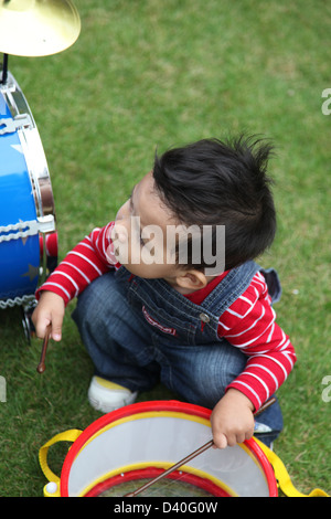 C'est une photo d'un jeune enfant garçon qui joue de la batterie sur un jouet enfant instrument musique batterie. C'est en bleu et sur l'herbe Banque D'Images