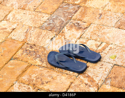 Tongs bleu childs jetés sur le pont pavé par piscine avec de l'eau dans des impressions Banque D'Images