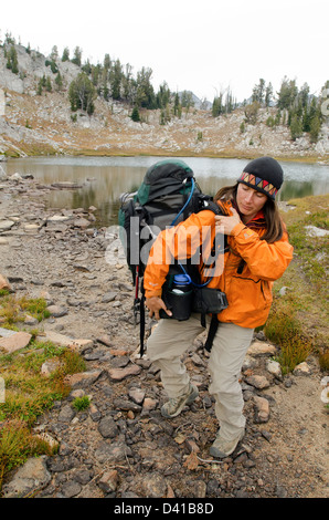 Woman putting sur un sac à dos dans les montagnes de l'Oregon Wallowa. Banque D'Images