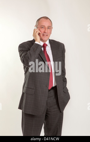 Homme mûr en 50s portant un costume gris, l'utilisation d'un cellulaire ou un téléphone mobile, à la recherche à l'appareil photo en souriant. Banque D'Images