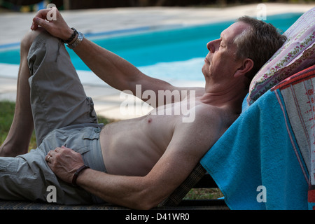 L'homme se détend à l'extérieur sur une serviette couverts à côté d'une chaise longue piscine. Banque D'Images