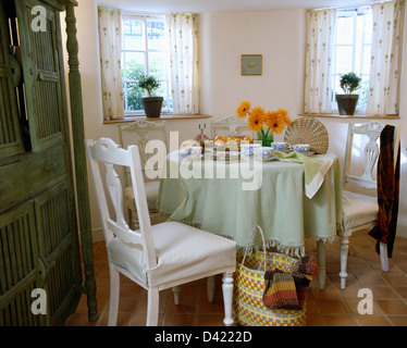 Meuble blanc couvre sur chaise de salle à manger à table avec un tissu vert pâle en salle à manger avec panier coloré sur marbre Banque D'Images